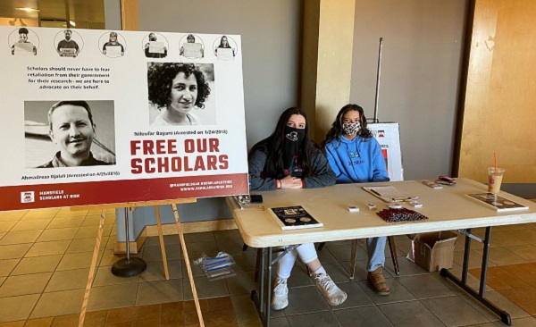 Two students next to a sign that says Free Our Scholars. Students are at a table giving out information.